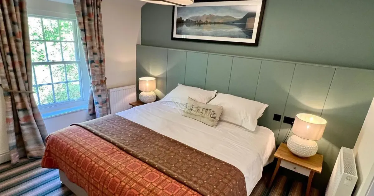 Cosy double bedroom with a green panelled feature wall, patterned bedspread and bedside lamps.