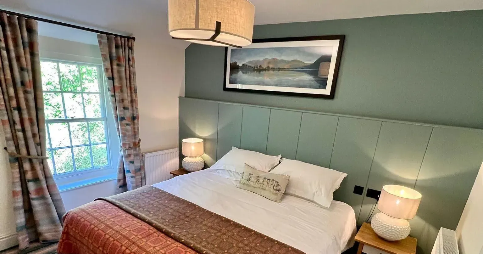 Cosy double bedroom with a green panelled feature wall, patterned bedspread and bedside lamps.