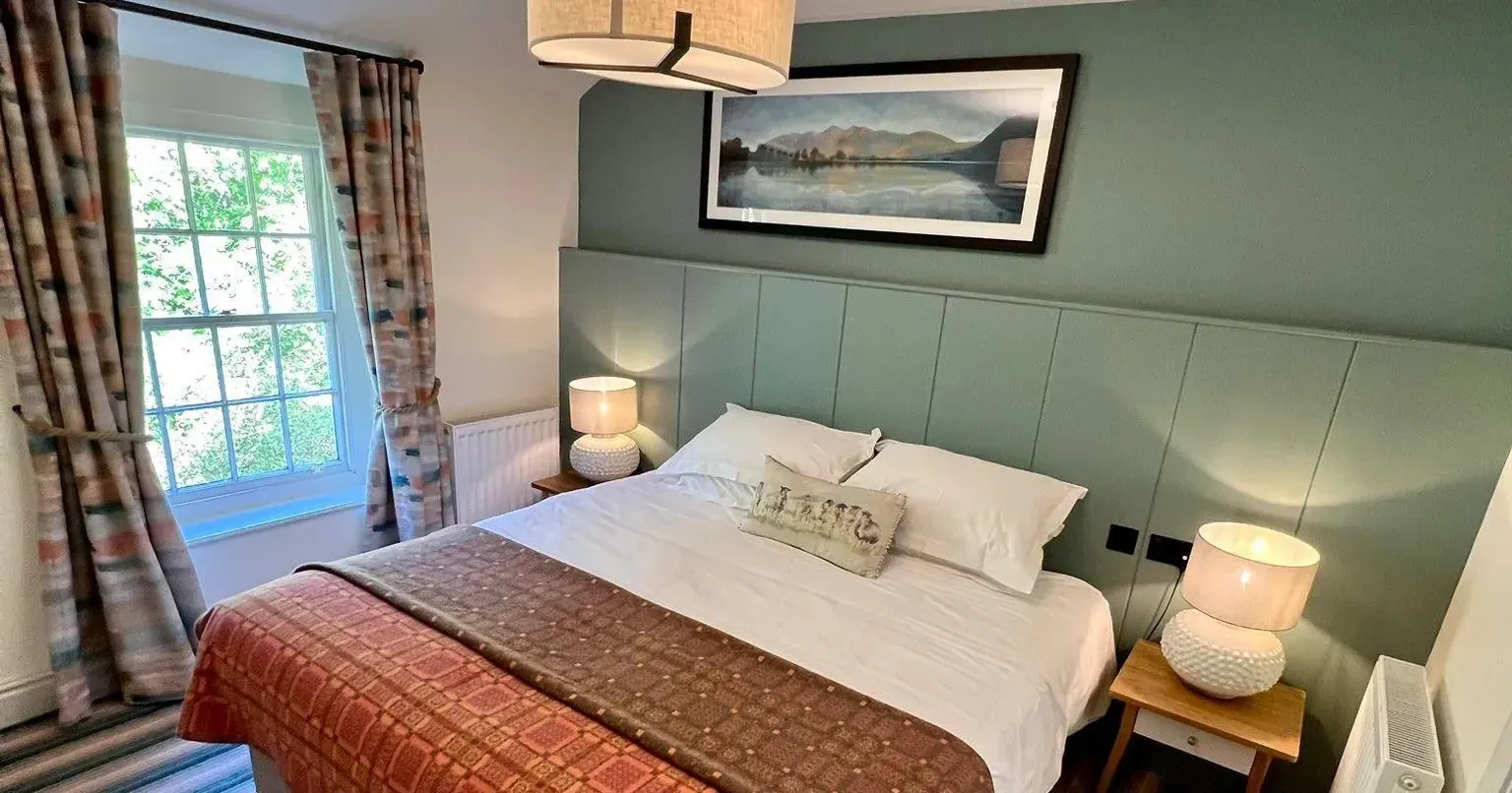 Cosy double bedroom with a green panelled feature wall, patterned bedspread and bedside lamps.