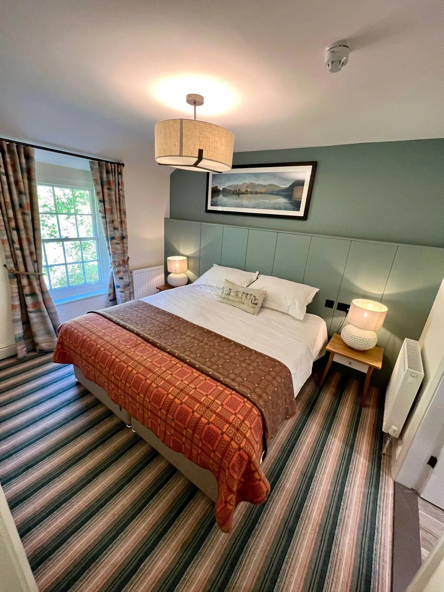 Cosy double bedroom with a green panelled feature wall, patterned bedspread and bedside lamps.