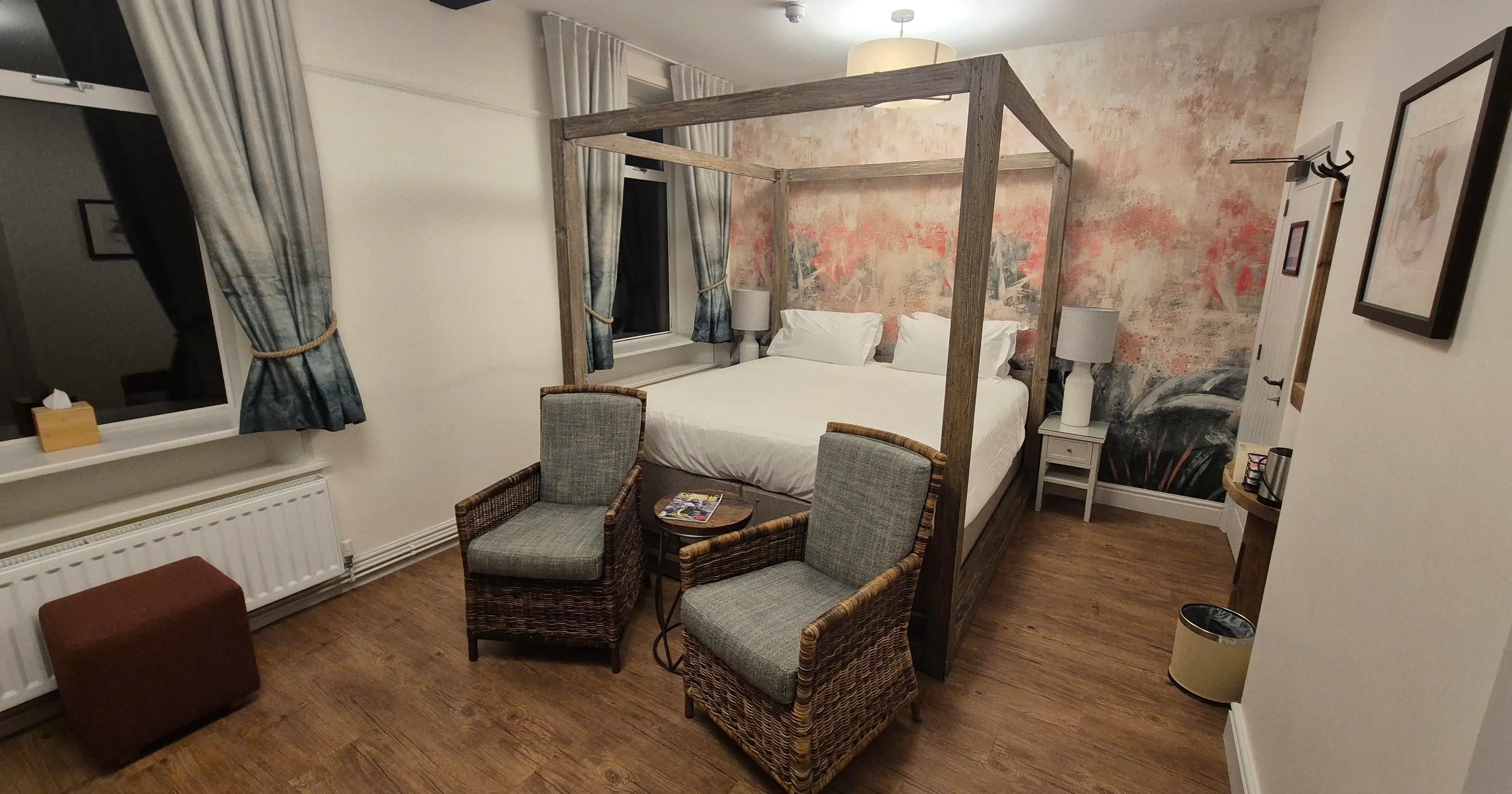 Cosy bedroom with a wooden four-poster bed, wicker armchairs and floral feature wall