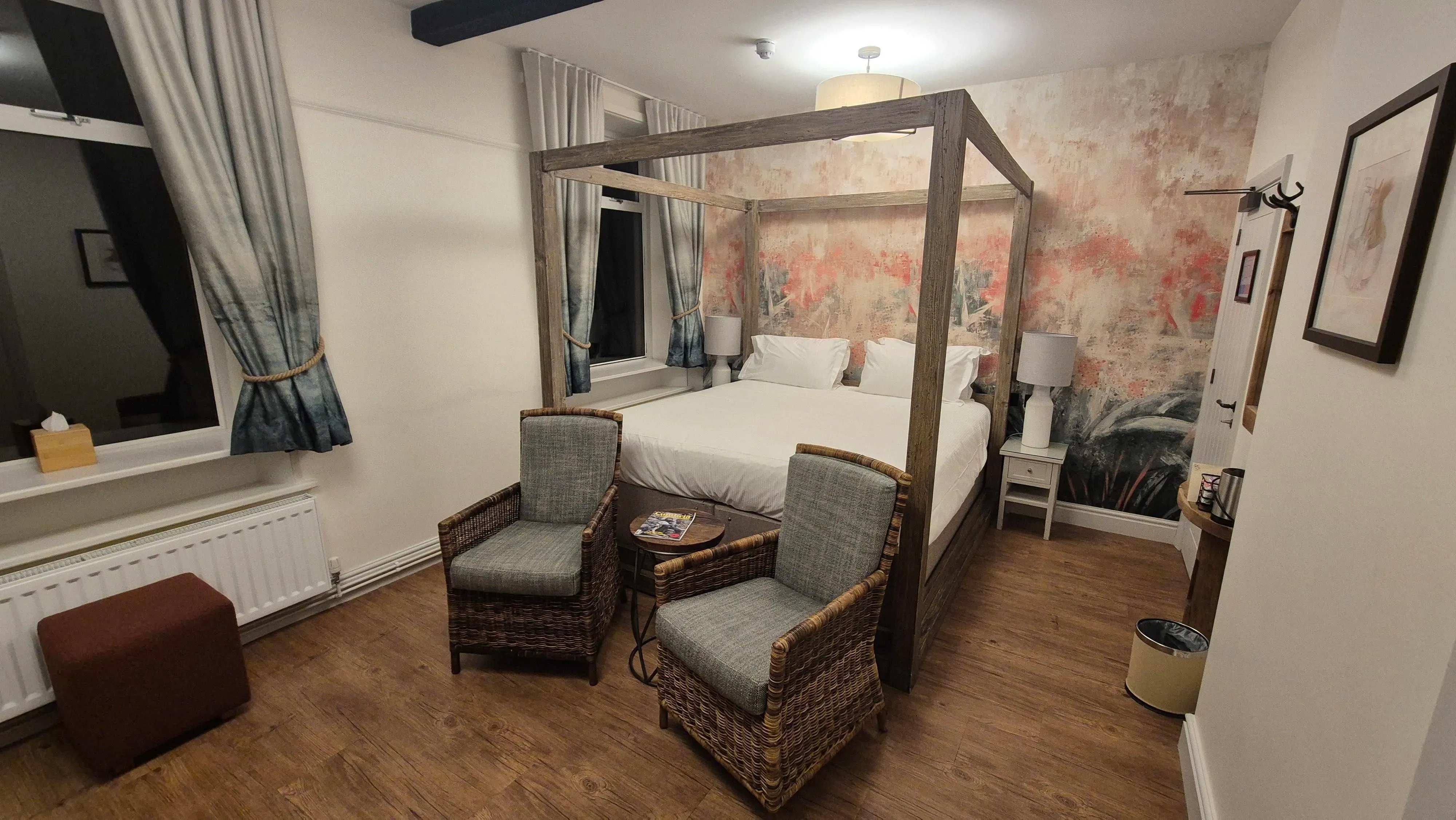 Cosy bedroom with a wooden four-poster bed, wicker armchairs and floral feature wall
