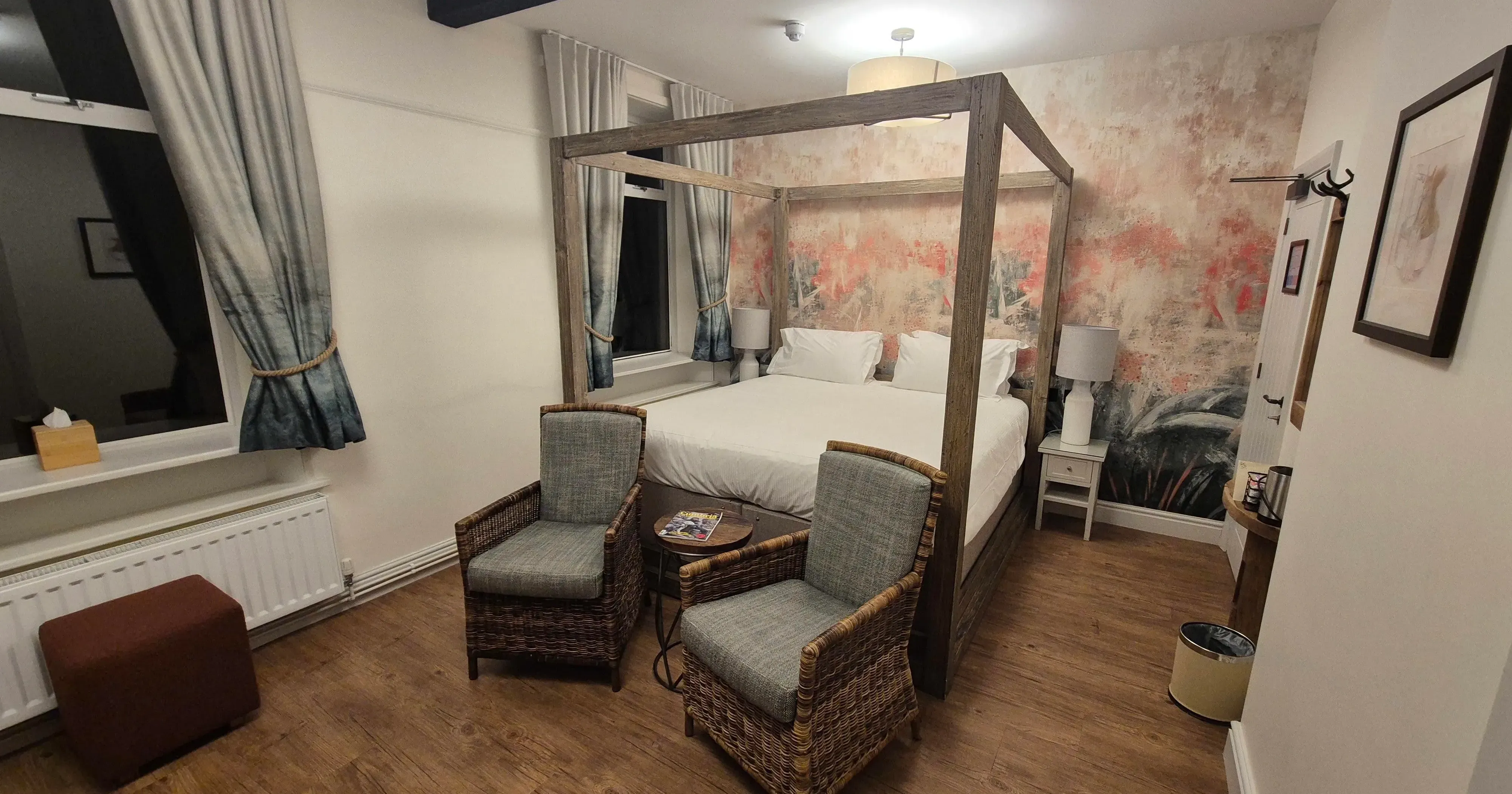 Cosy bedroom with a wooden four-poster bed, wicker armchairs and floral feature wall