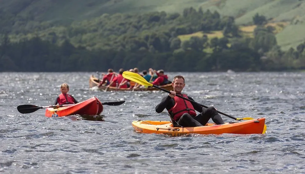Man and child kayaking on a lake with a canoe group behind them