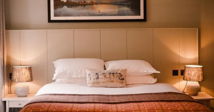 Cosy bedroom with a double bed, warm bedside lamps and framed landscape artwork.