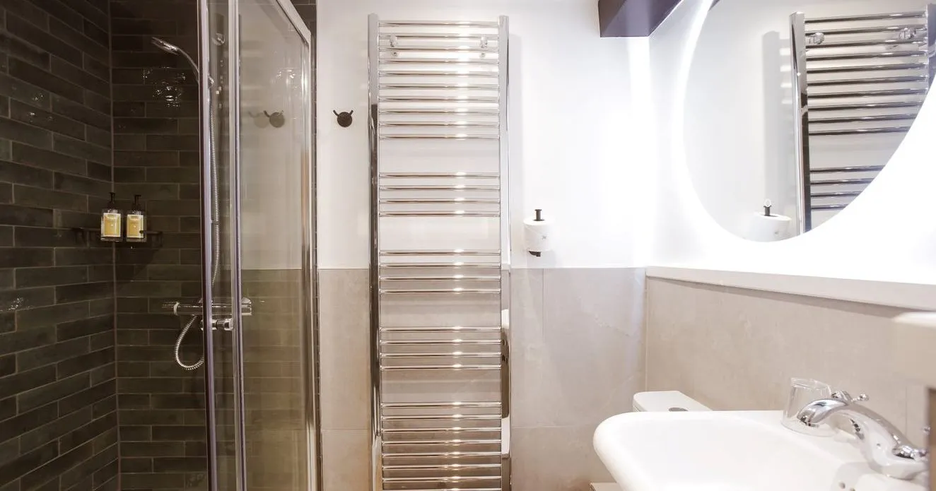 Modern bathroom with glass shower, dark tiled wall, chrome towel radiator and white basin