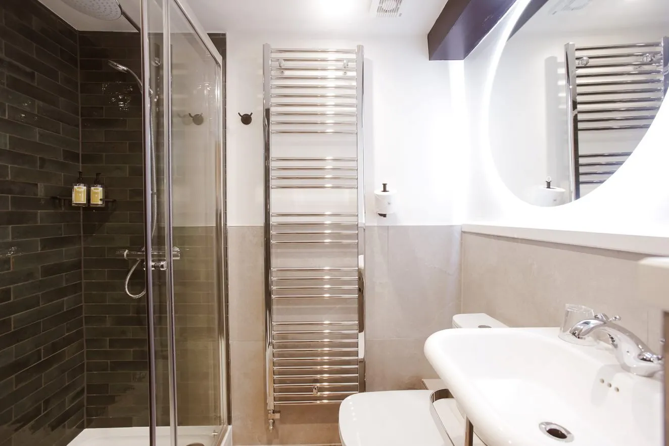 Modern bathroom with glass shower, dark tiled wall, chrome towel radiator and white basin