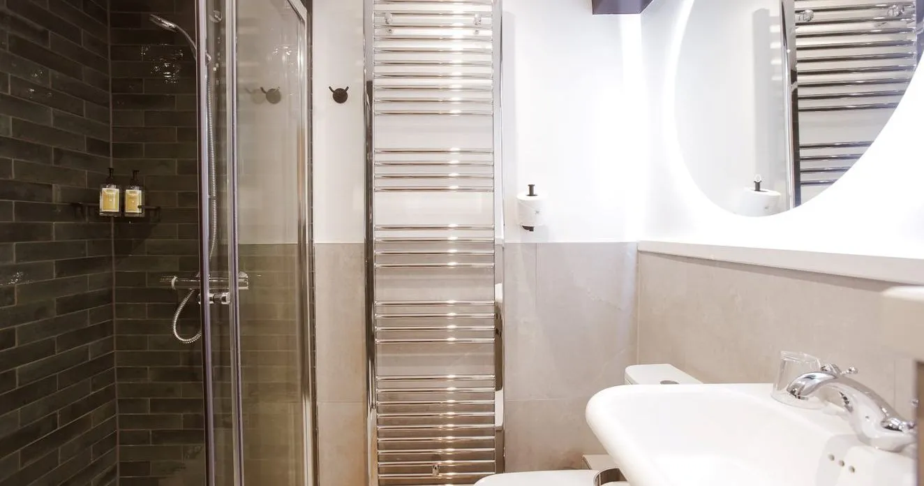 Modern bathroom with glass shower, dark tiled wall, chrome towel radiator and white basin