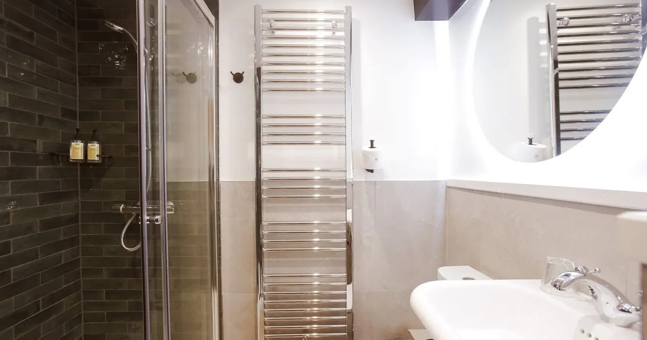 Modern bathroom with glass shower, dark tiled wall, chrome towel radiator and white basin