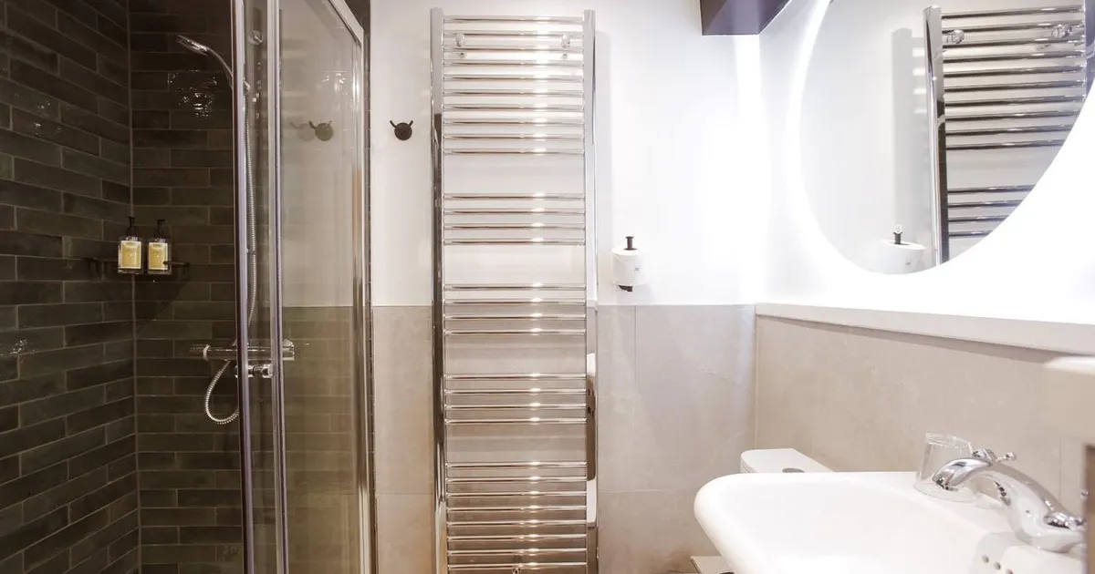 Modern bathroom with glass shower, dark tiled wall, chrome towel radiator and white basin