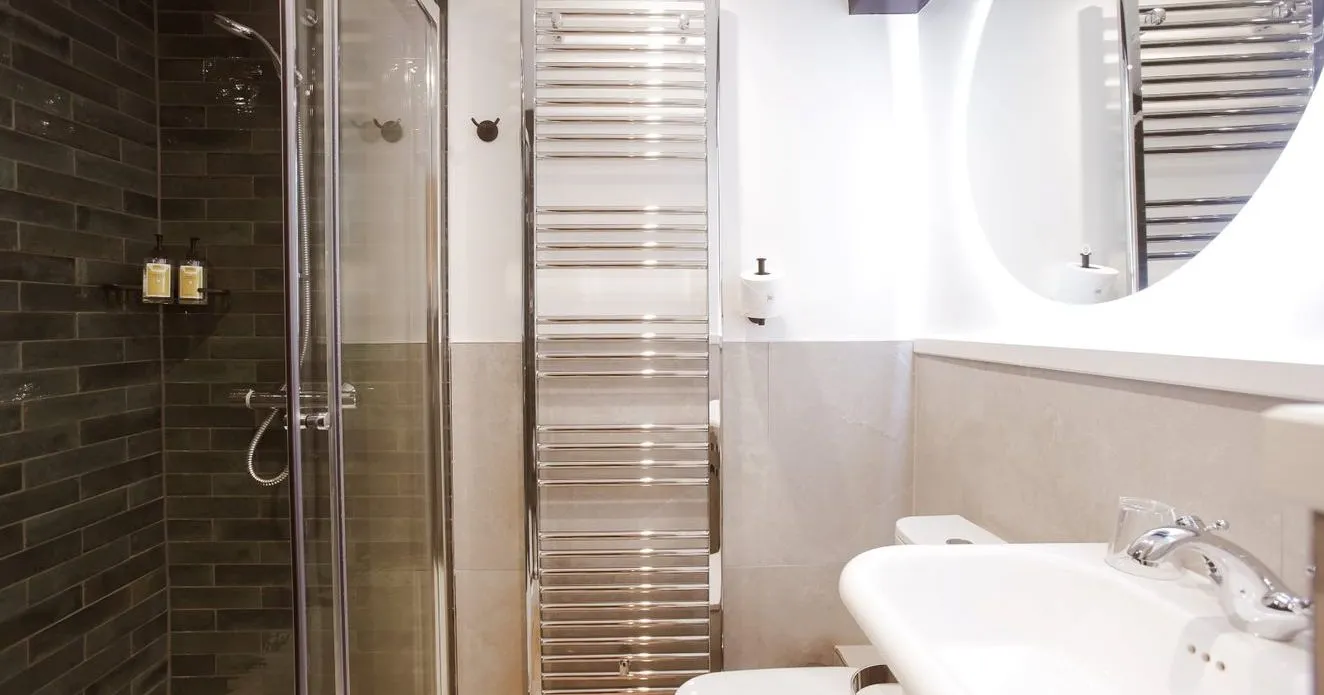Modern bathroom with glass shower, dark tiled wall, chrome towel radiator and white basin
