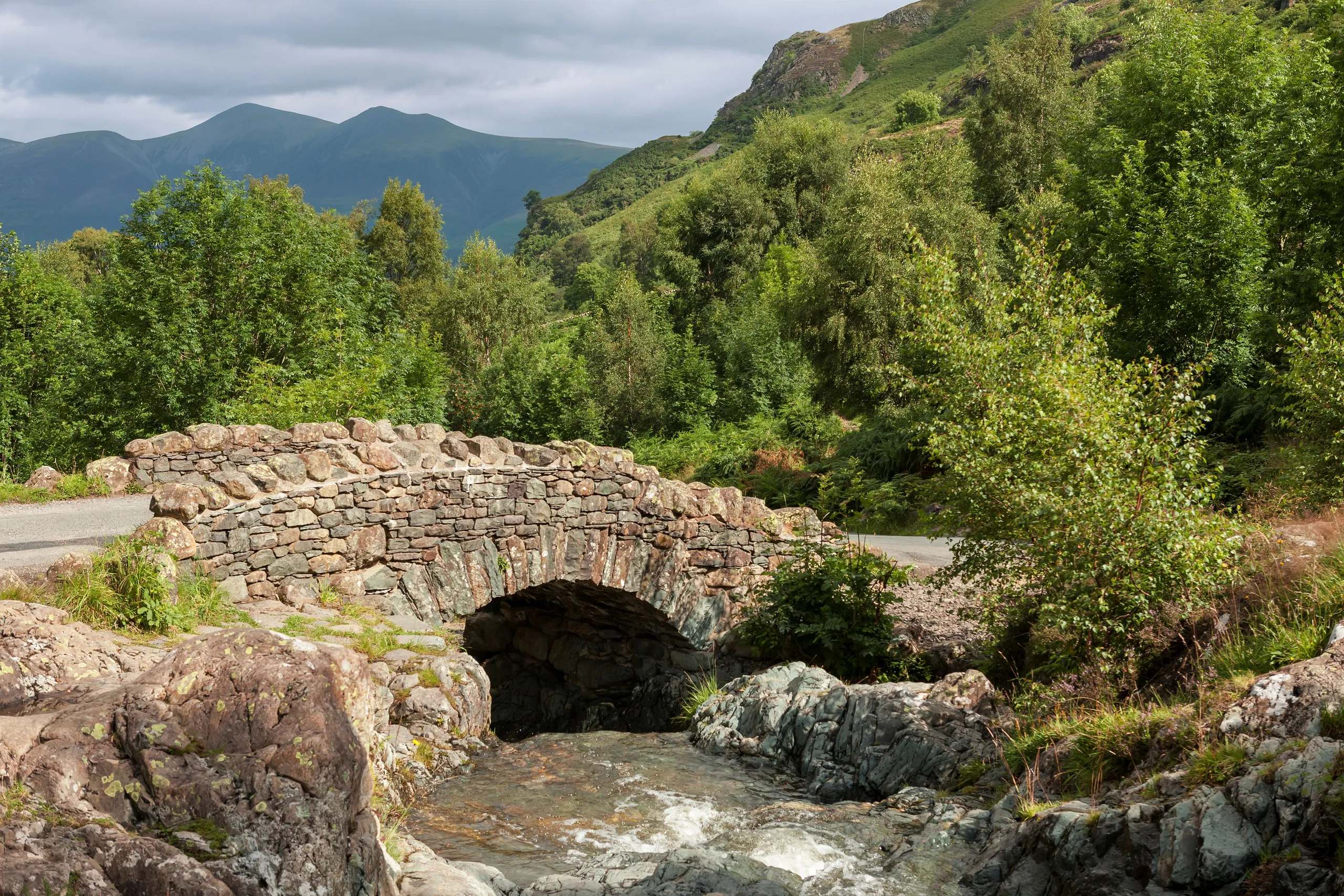 Historic stone arch bridge over a rocky stream in a lush mountain valley