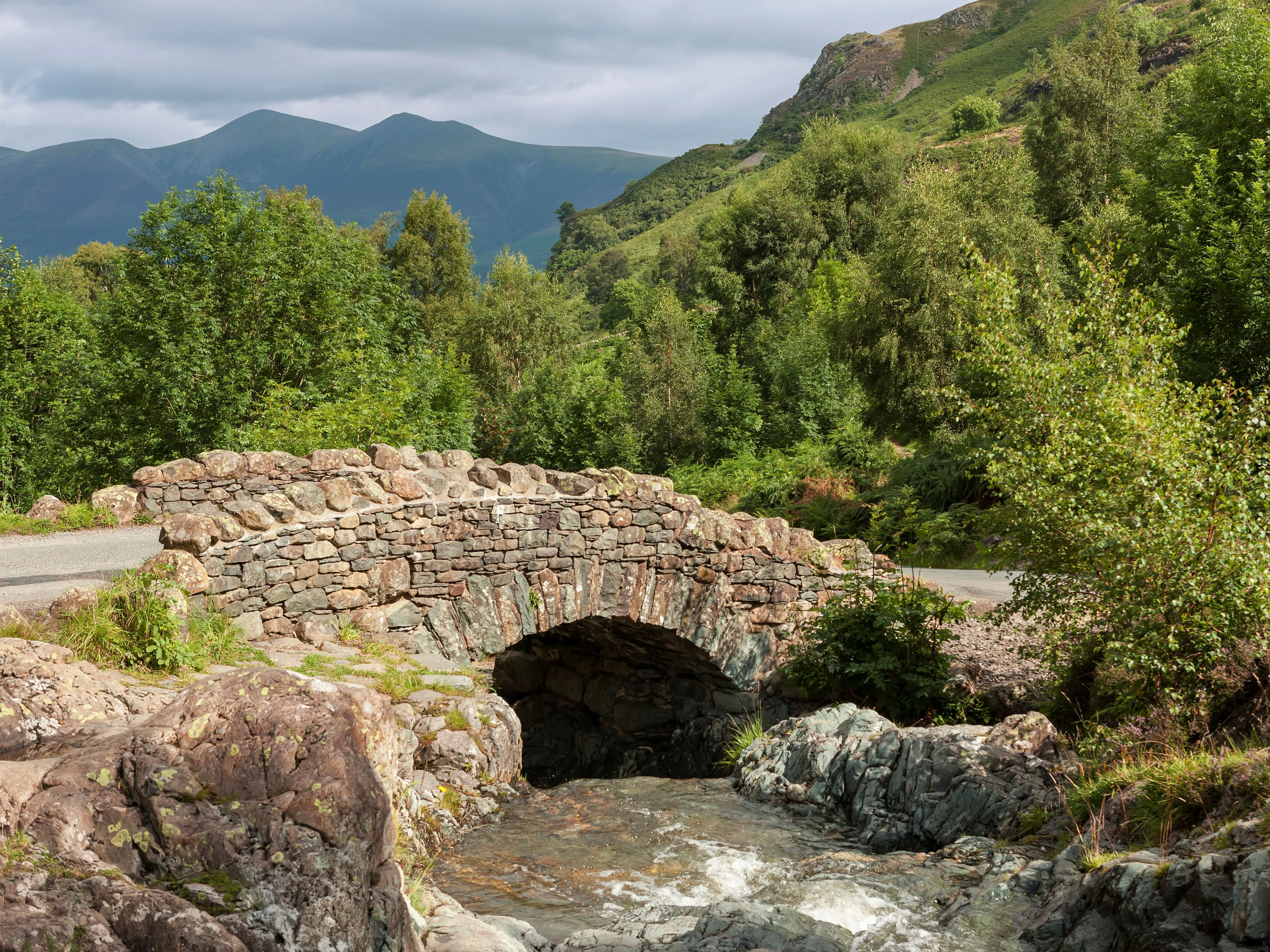 Historic stone arch bridge over a rocky stream in a lush mountain valley