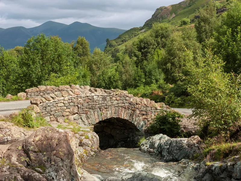 Historic stone arch bridge over a rocky stream in a lush mountain valley