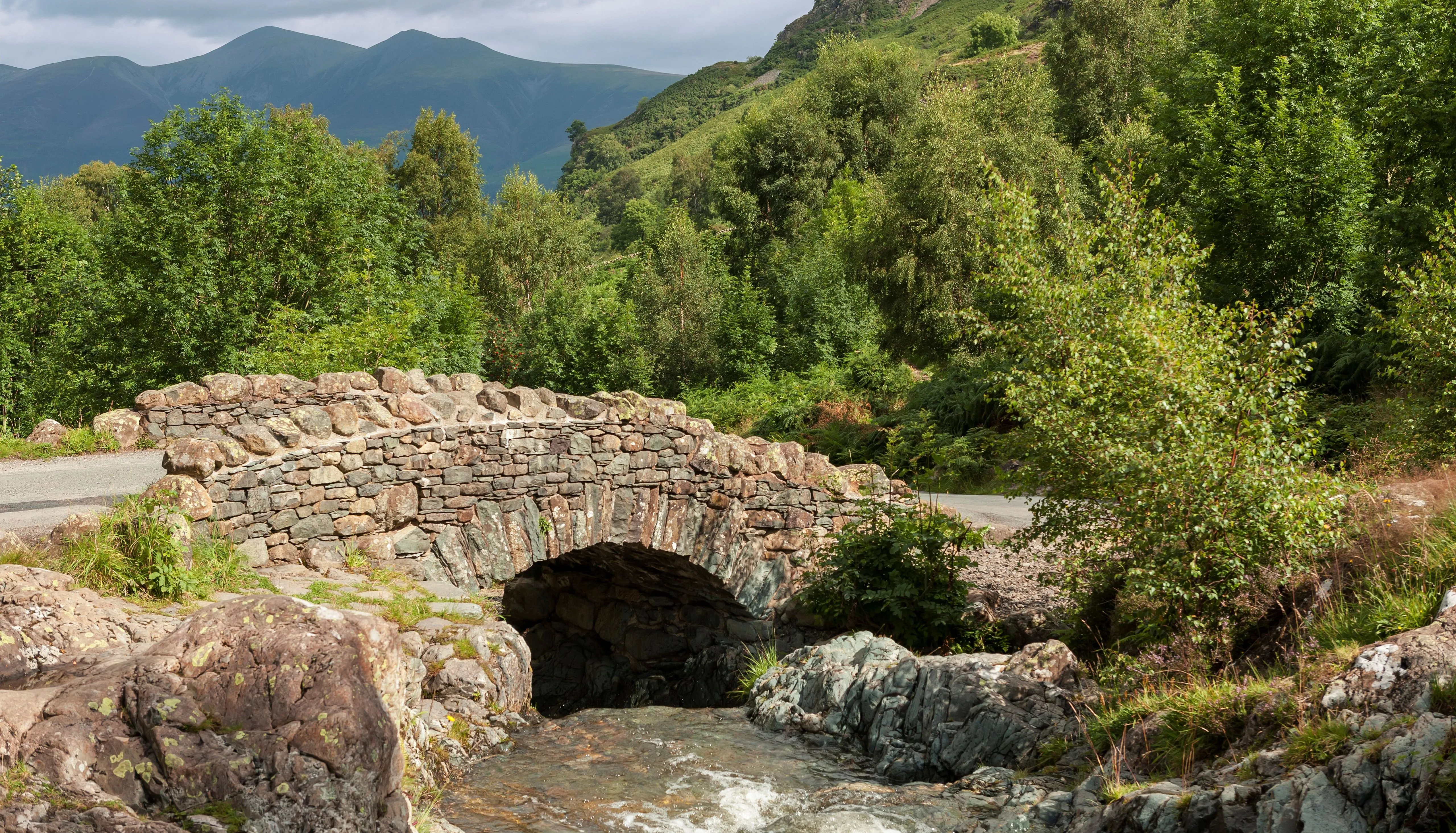 Historic stone arch bridge over a rocky stream in a lush mountain valley