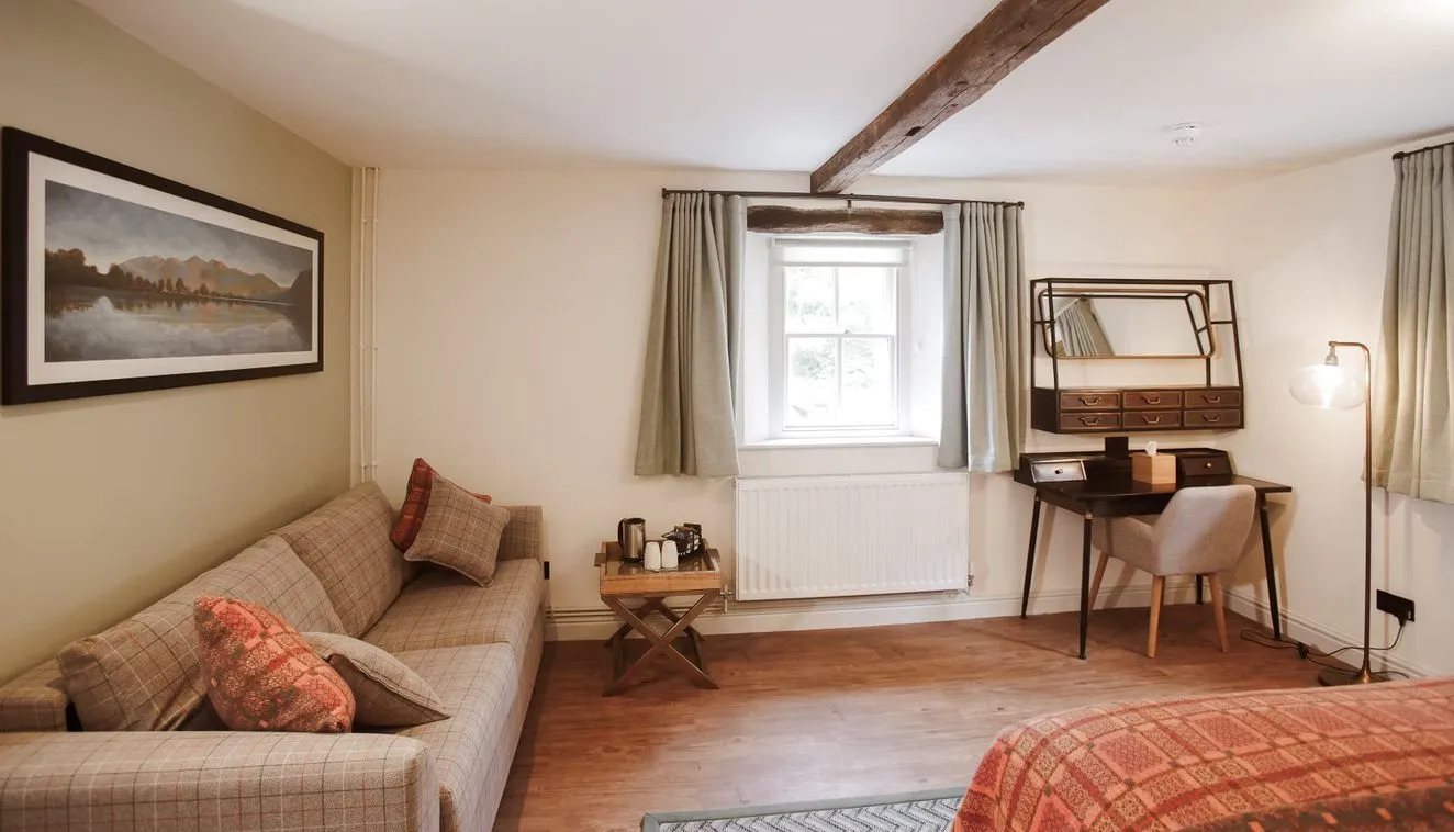 Cosy bedroom with a checked sofa, writing desk, exposed wooden beams and patterned bedspread.