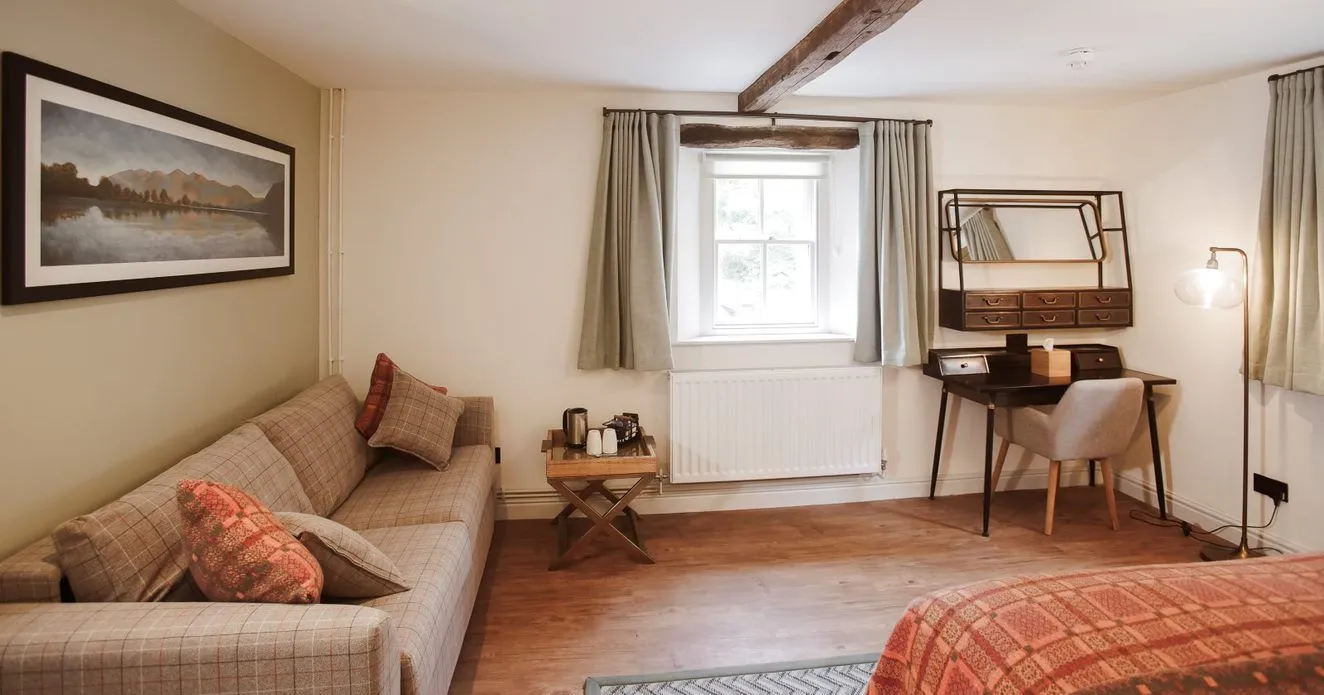 Cosy bedroom with a checked sofa, writing desk, exposed wooden beams and patterned bedspread.