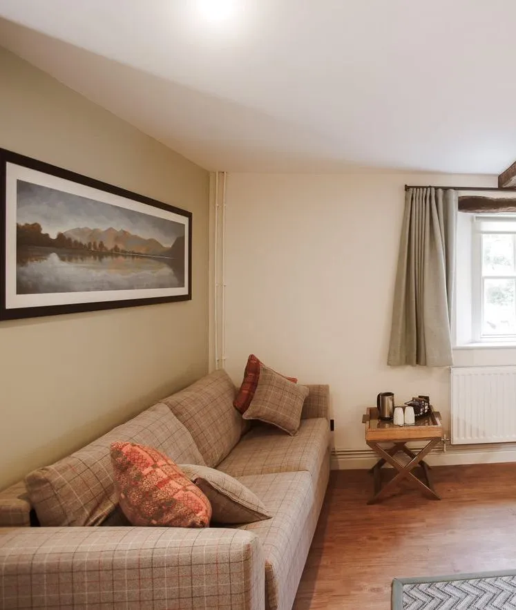 Cosy bedroom with a checked sofa, writing desk, exposed wooden beams and patterned bedspread.