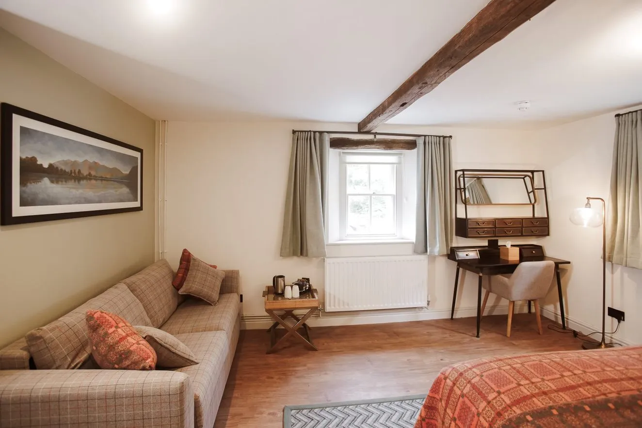 Cosy bedroom with a checked sofa, writing desk, exposed wooden beams and patterned bedspread.