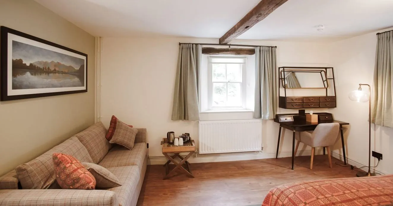 Cosy bedroom with a checked sofa, writing desk, exposed wooden beams and patterned bedspread.
