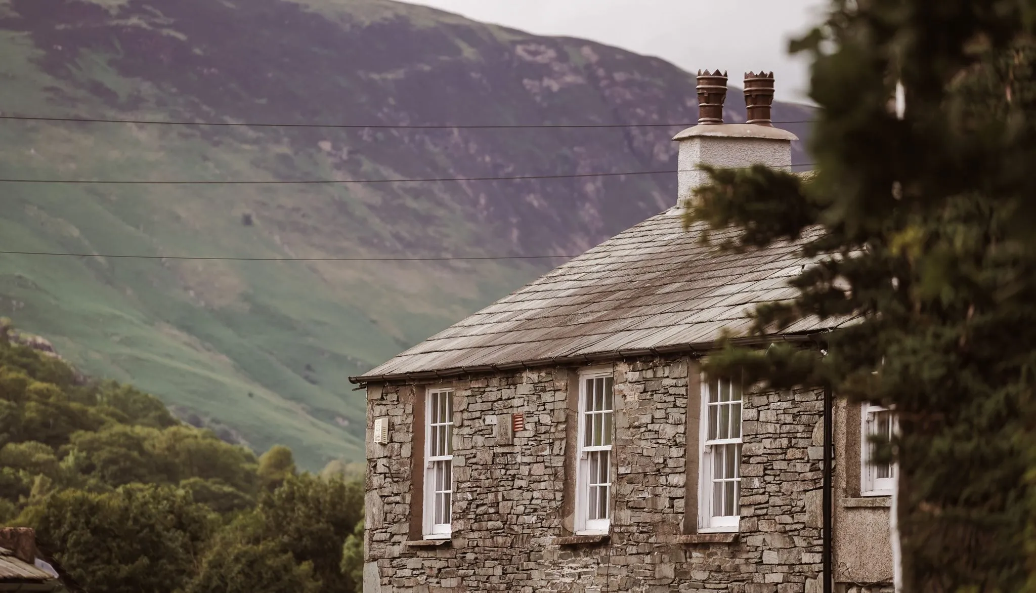 Traditional stone cottage with a slate roof set against a green mountain valley