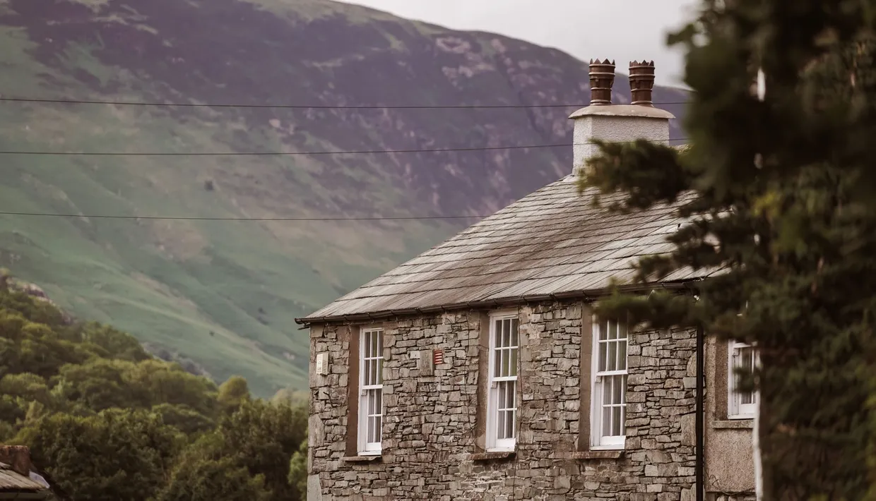 Traditional stone cottage with a slate roof set against a green mountain valley