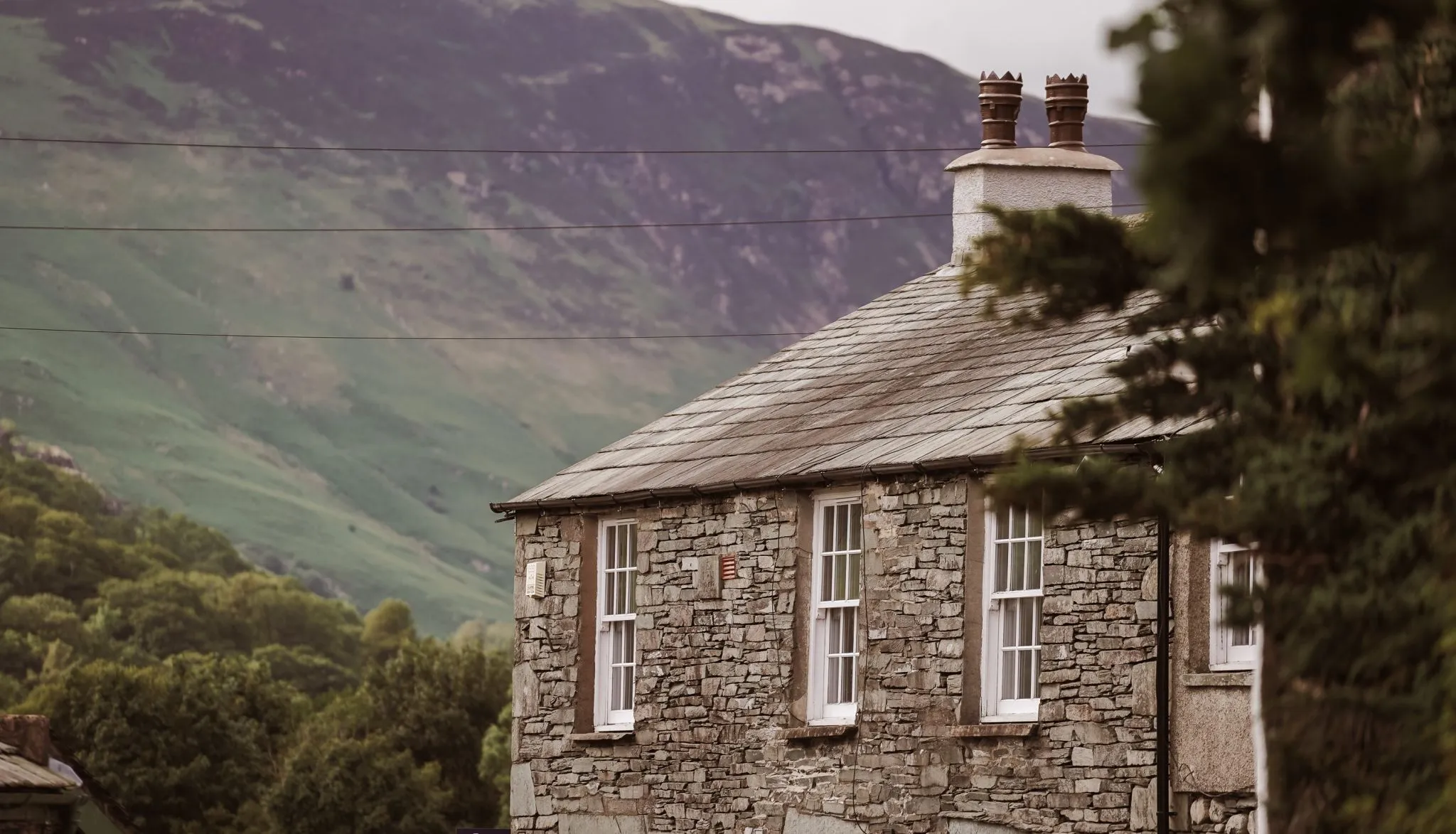 Traditional stone cottage with a slate roof set against a green mountain valley