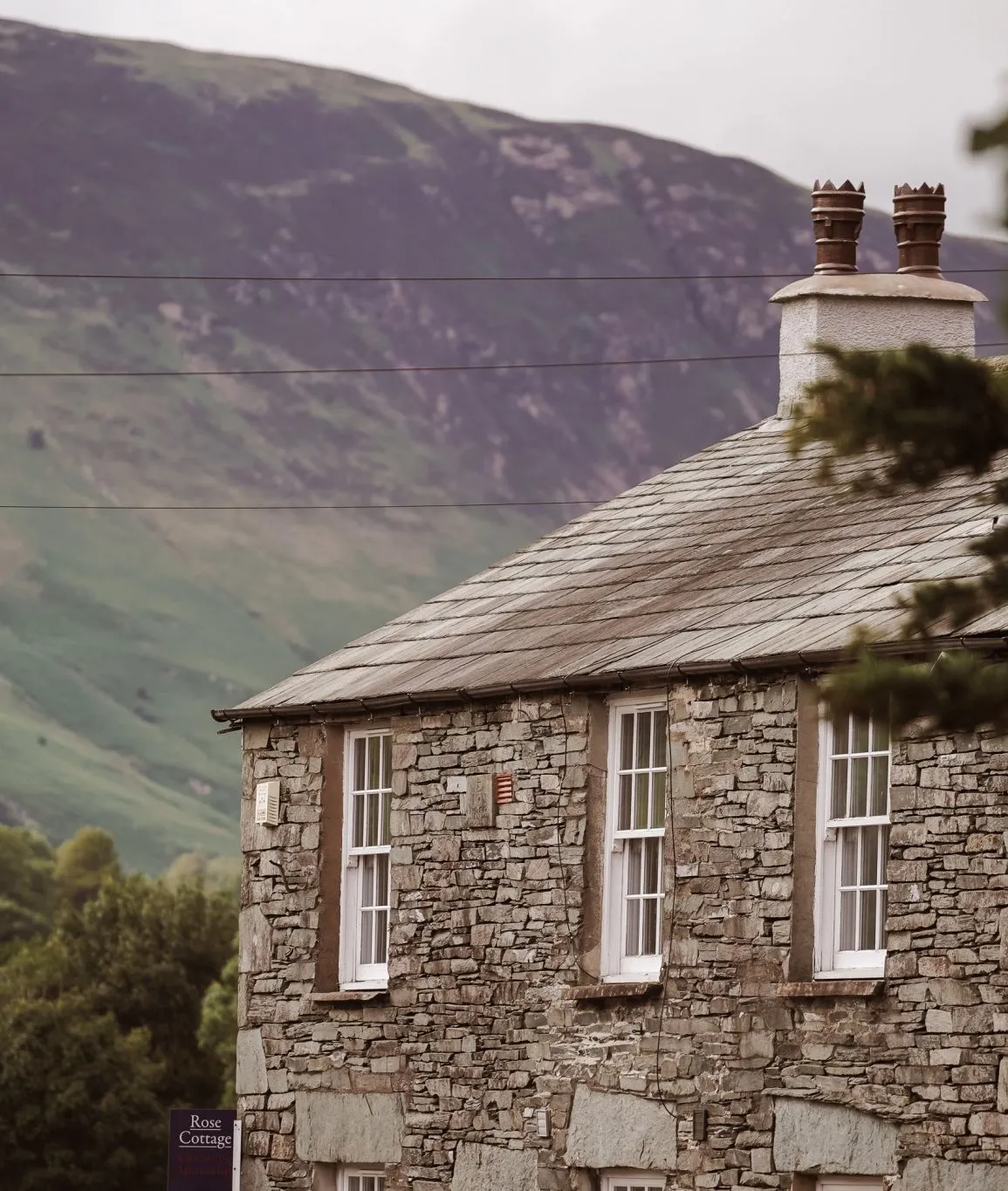 Traditional stone cottage with a slate roof set against a green mountain valley