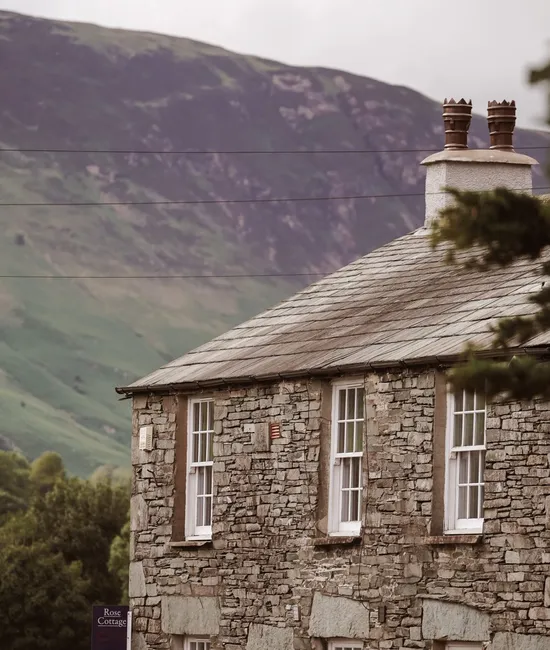 Traditional stone cottage with a slate roof set against a green mountain valley