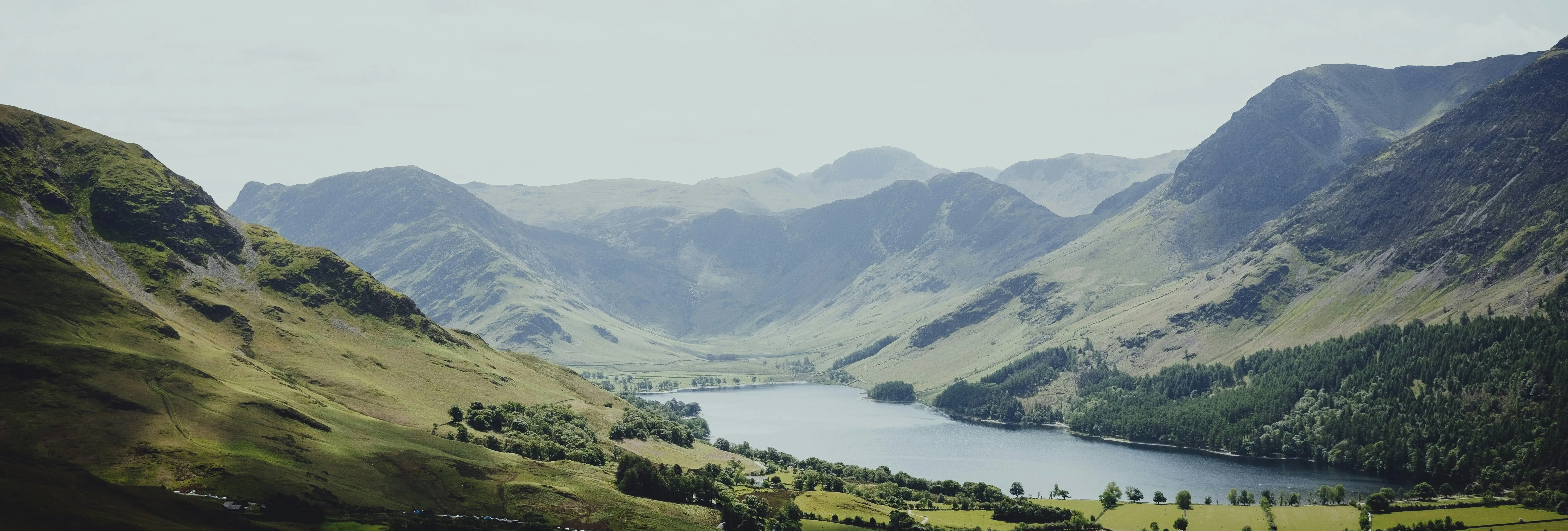 Panoramic view of a lake nestled between green mountains beneath a cloudy sky