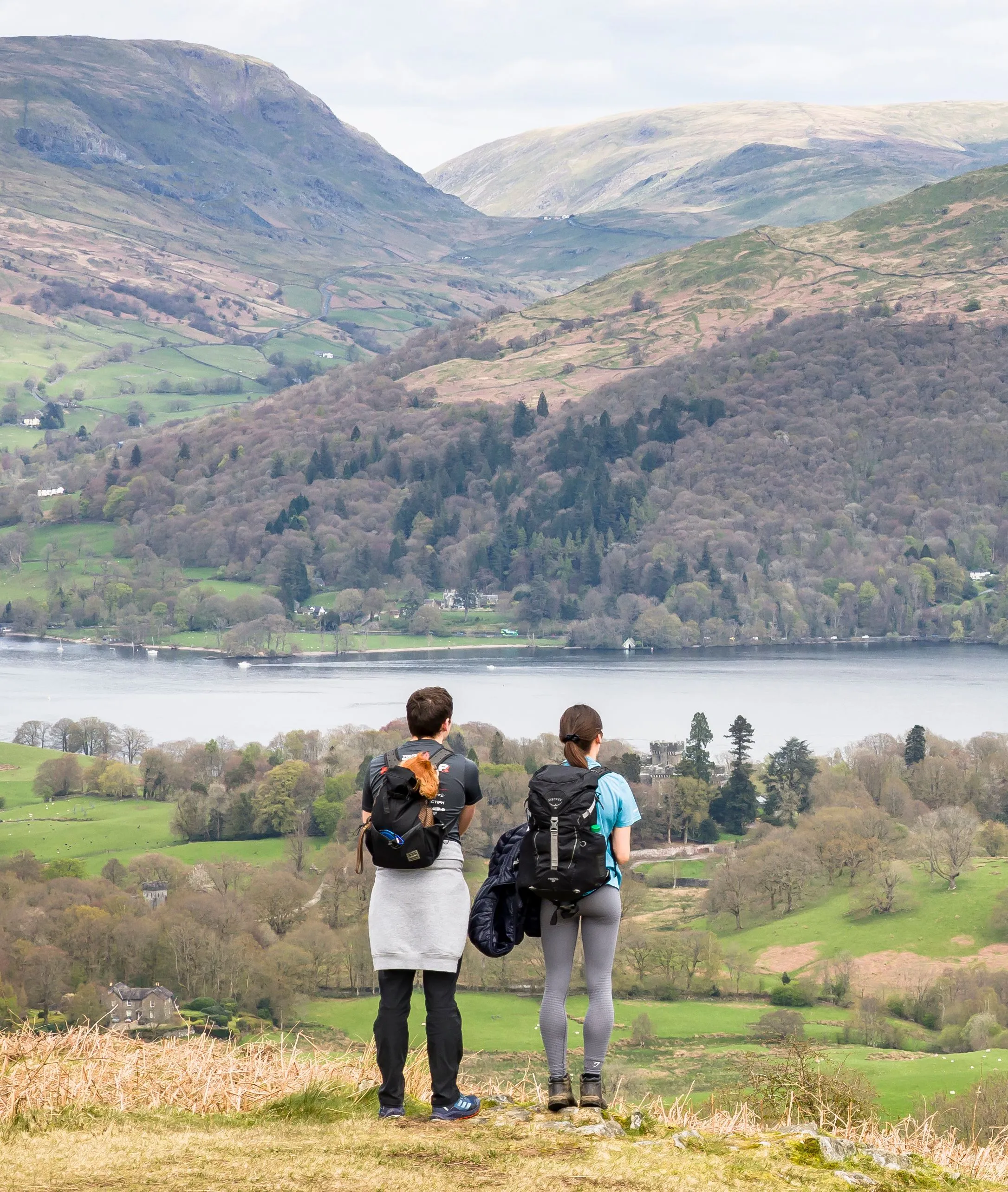 Two hikers with backpacks overlooking a lake and green mountain valley.
