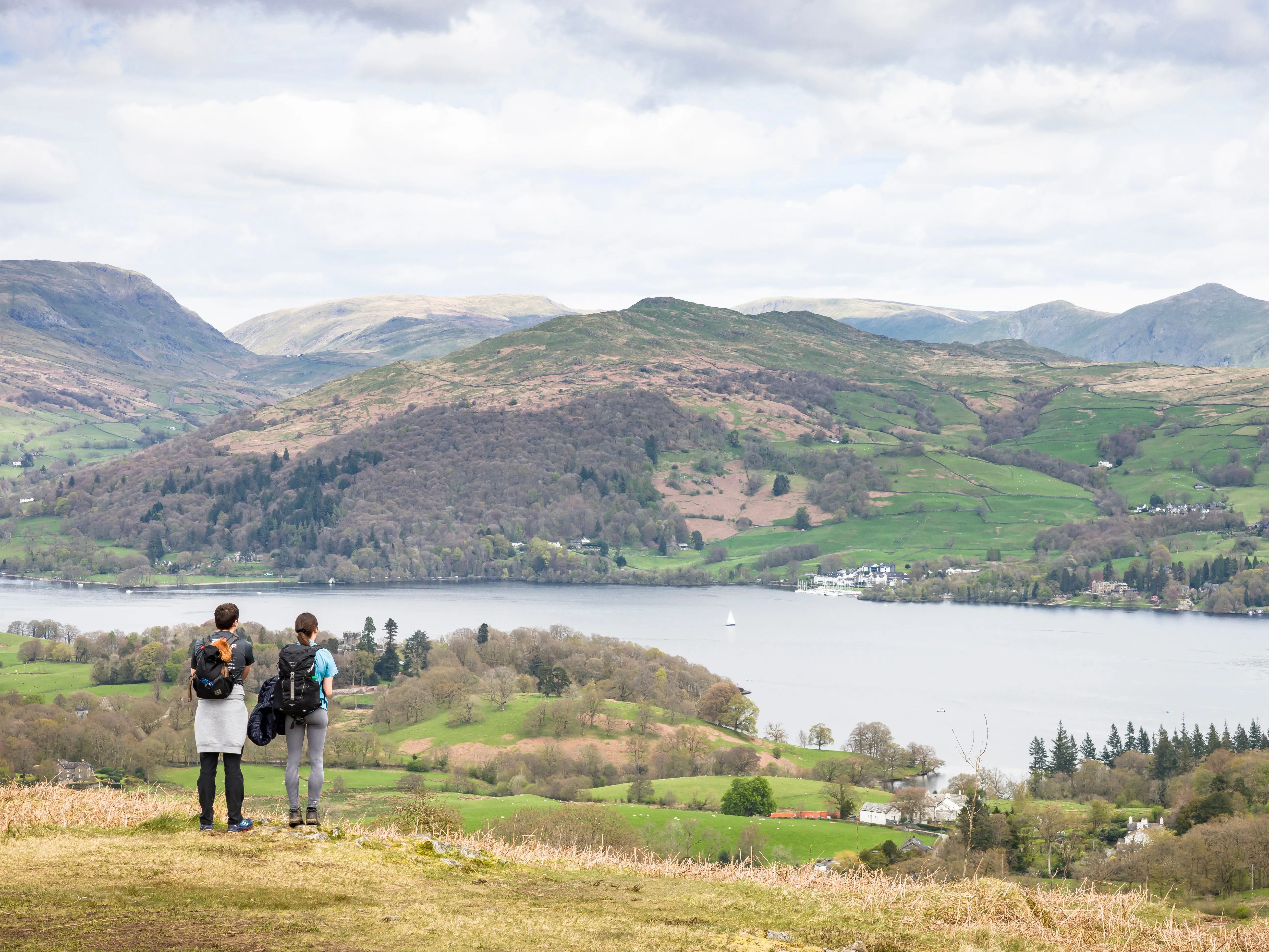 Two hikers with backpacks overlooking a lake and green mountain valley.