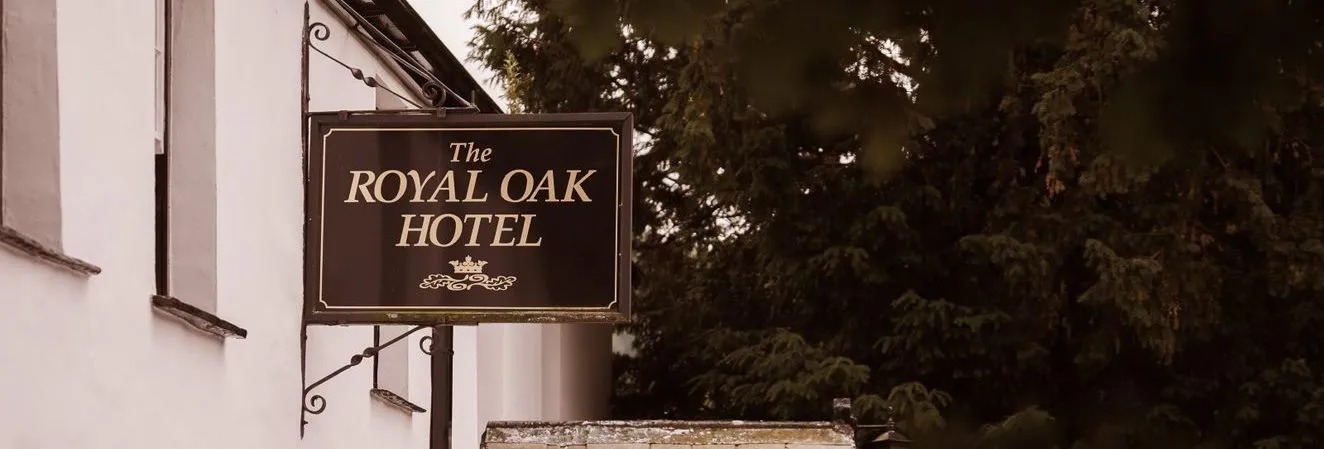 Hanging sign for The Royal Oak Hotel outside a white traditional building beside leafy trees.