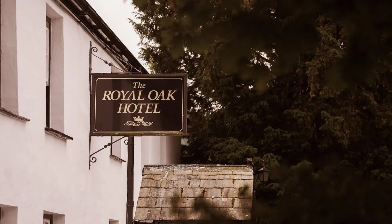 Hanging sign for The Royal Oak Hotel outside a white traditional building beside leafy trees.