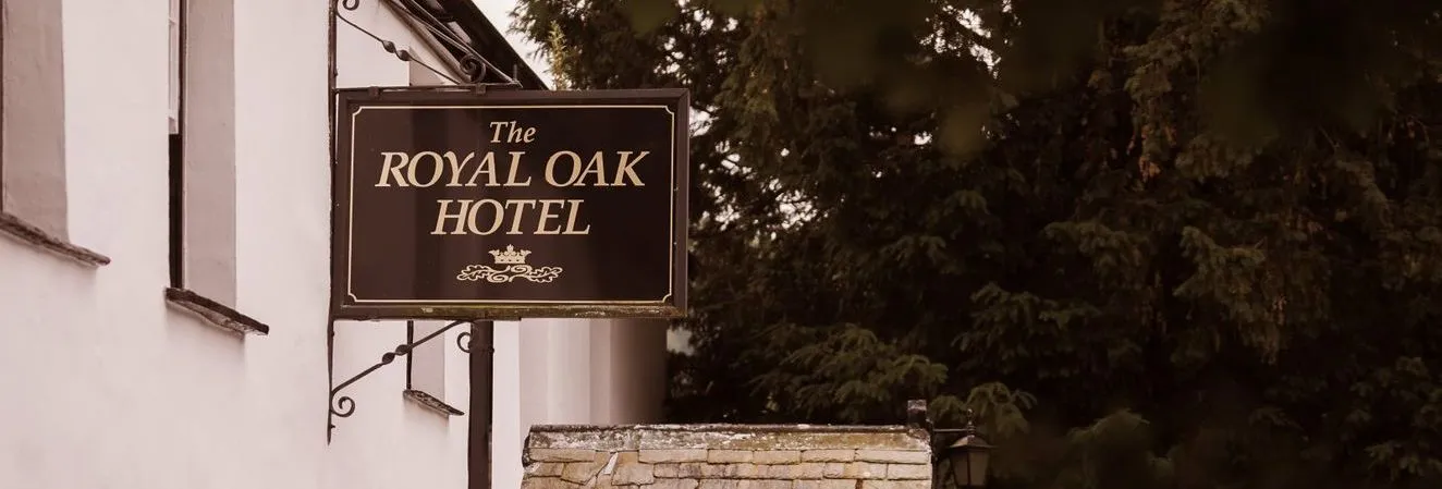 Hanging sign for The Royal Oak Hotel outside a white traditional building beside leafy trees.