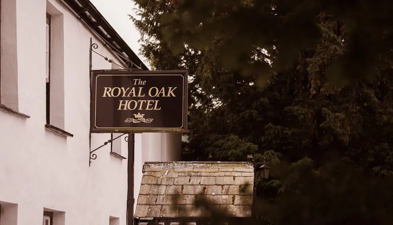Hanging sign for The Royal Oak Hotel outside a white traditional building beside leafy trees.