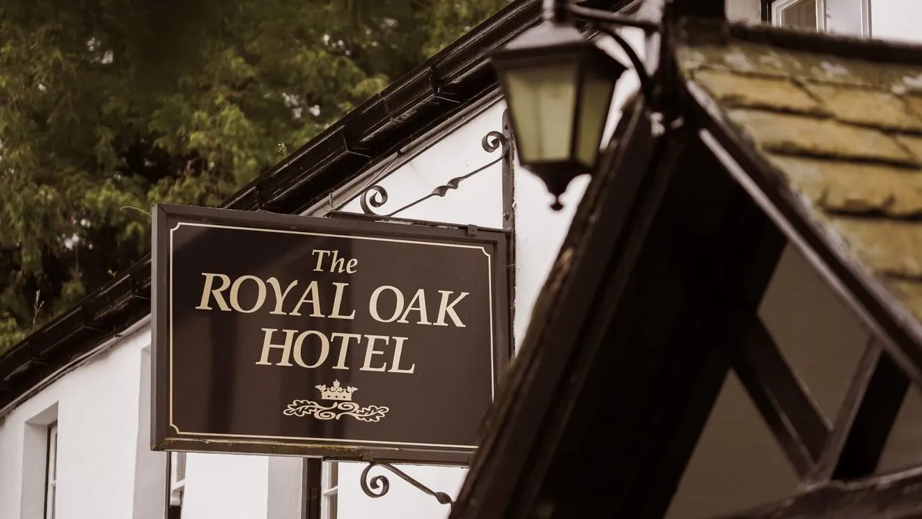 Sign for The Royal Oak Hotel hanging outside a traditional building with a lantern and leafy trees behind
