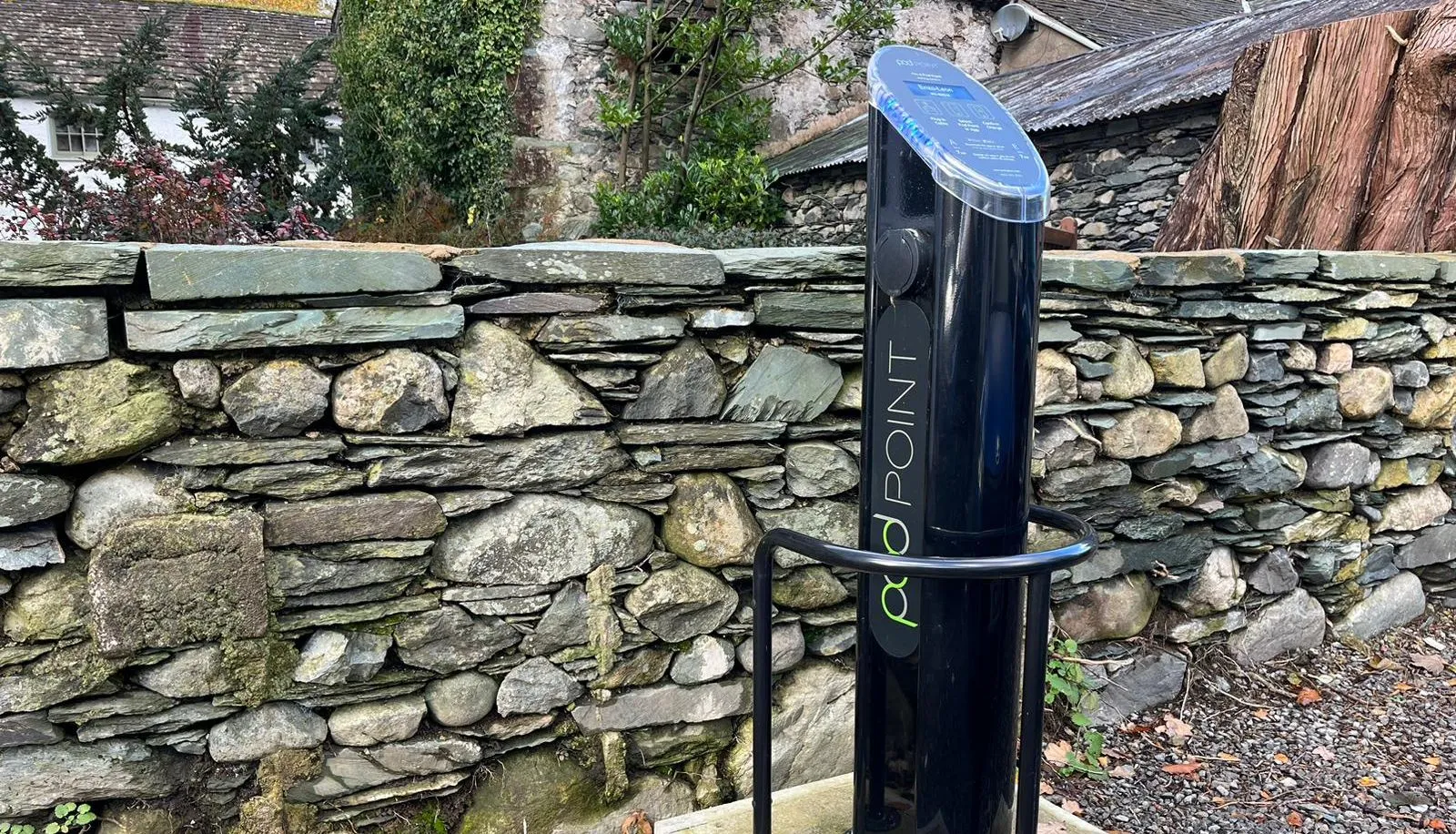 Black electric vehicle charging point beside a traditional stone wall