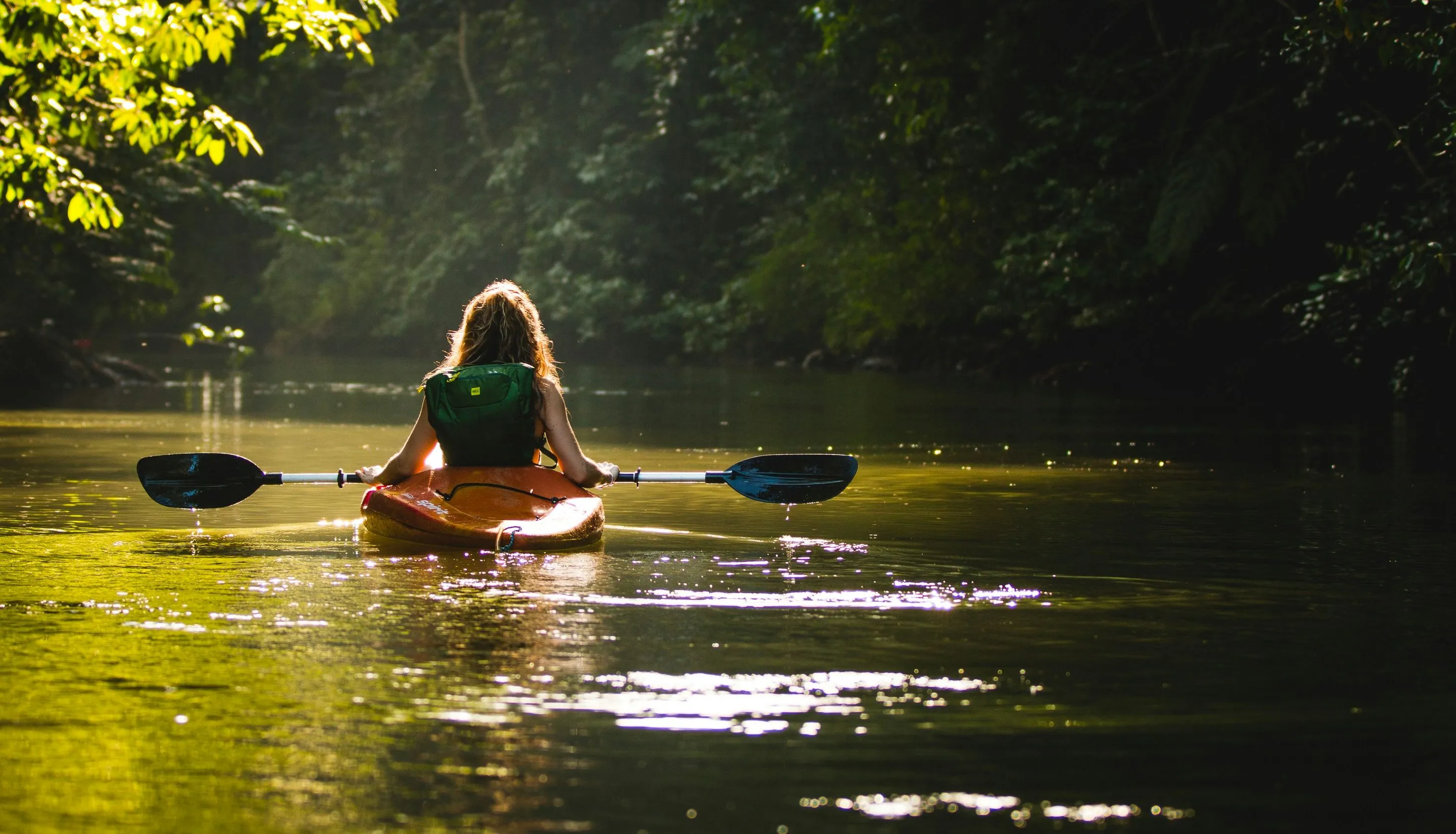 Person kayaking on a calm forest river in warm sunlight