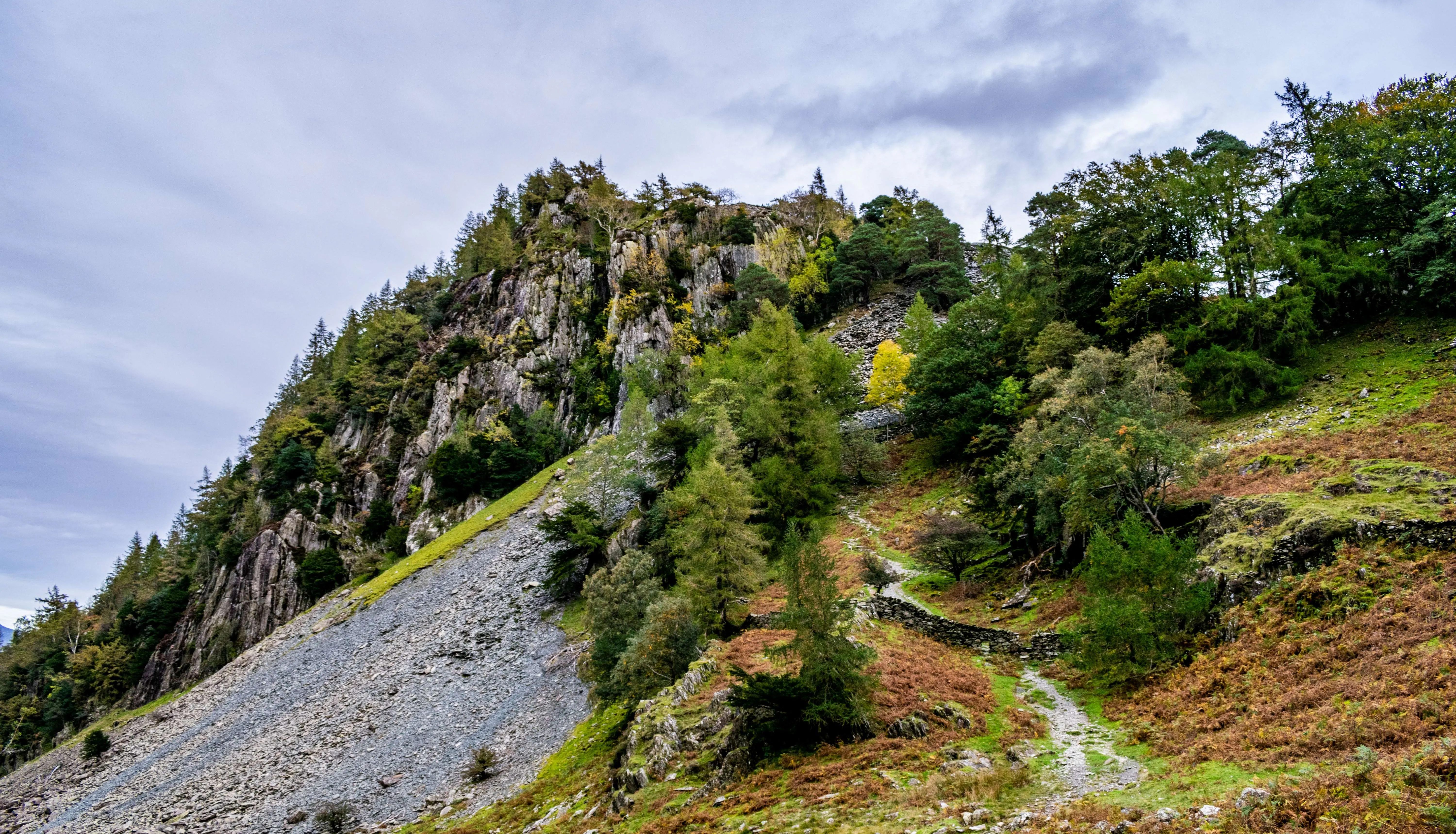 Rocky, tree-covered hillside with a winding footpath beneath an overcast sky.