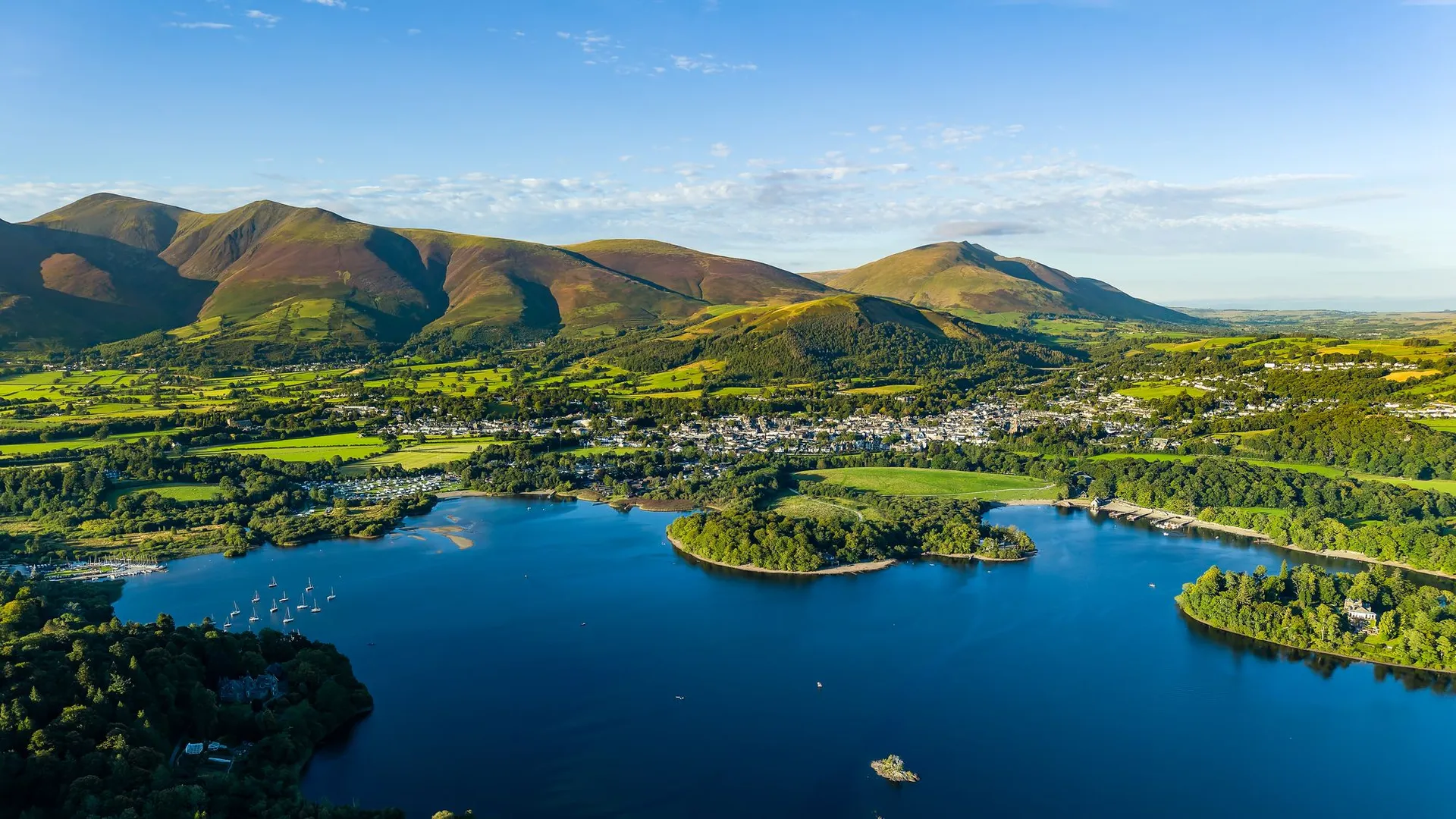 Aerial view of Derwent water lake, Keswick and the fells of the Lake District under a clear blue sky.