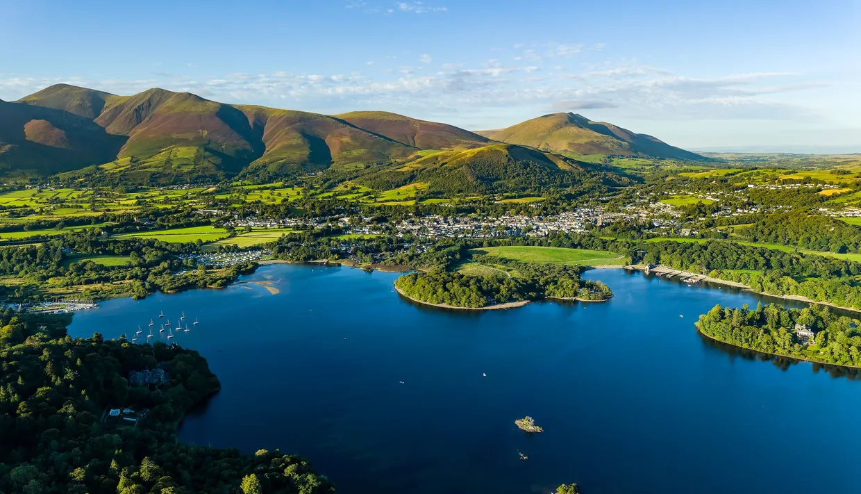 Aerial view of Derwent water lake, Keswick and the fells of the Lake District under a clear blue sky.