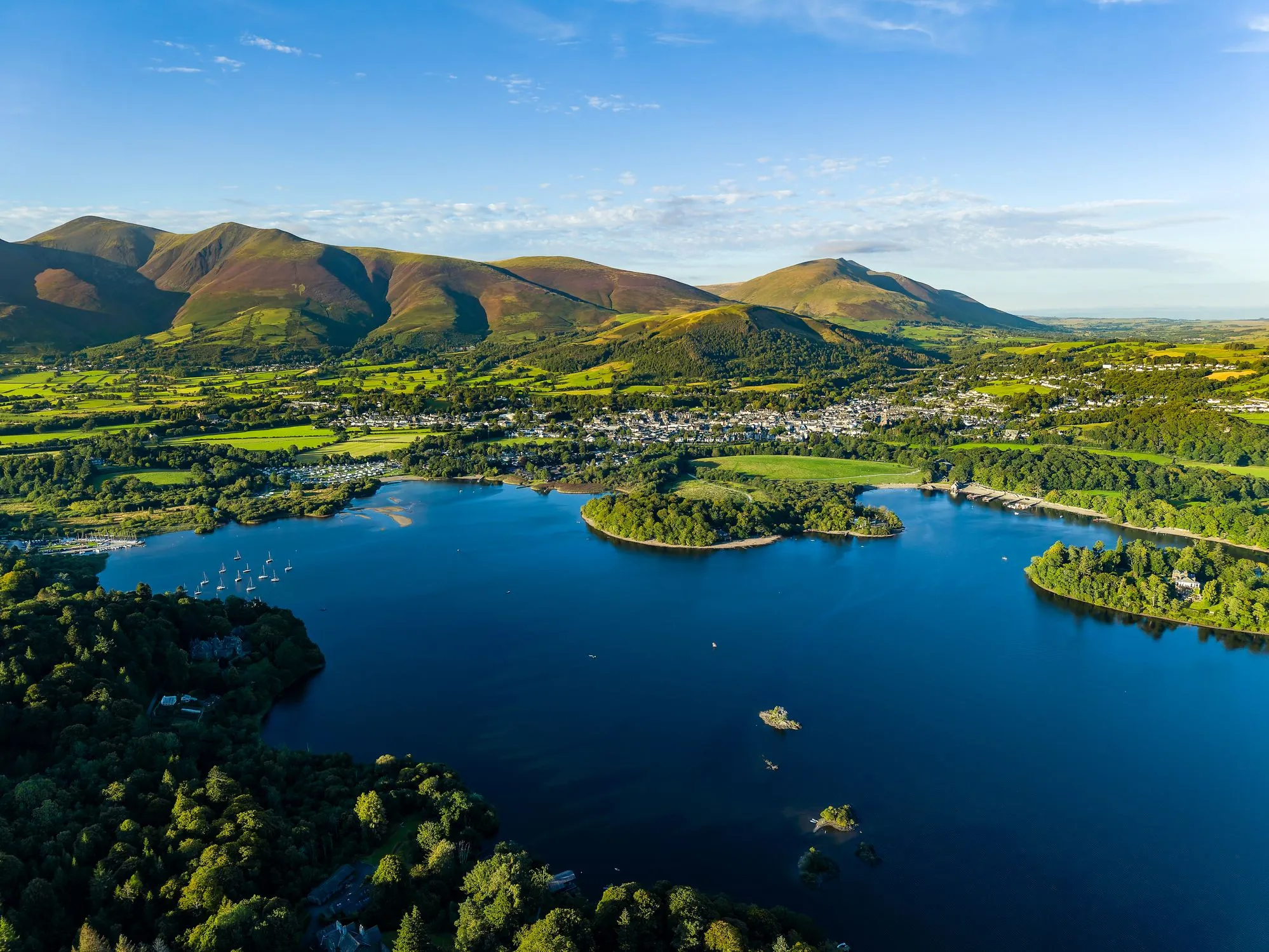 Aerial view of Derwent water lake, Keswick and the fells of the Lake District under a clear blue sky.