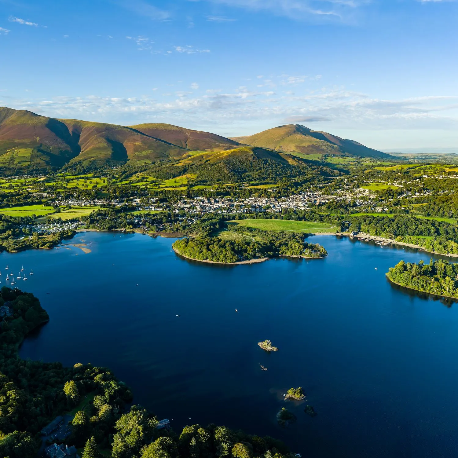 Aerial view of Derwent water lake, Keswick and the fells of the Lake District under a clear blue sky.