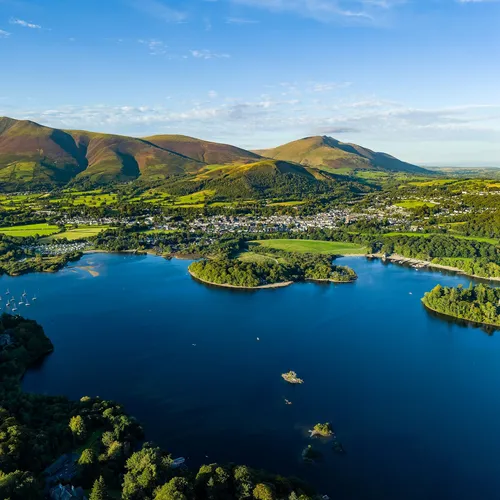 Aerial view of Derwent water lake, Keswick and the fells of the Lake District under a clear blue sky.