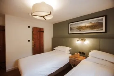 Warmly lit twin bedroom with two single beds, a bedside table and framed landscape artwork.