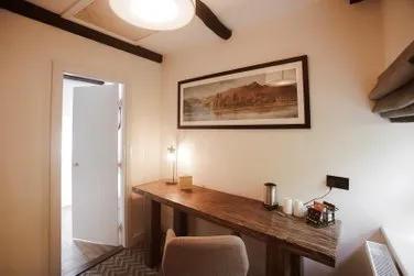 Warmly lit home office with a long wooden desk, chair, framed landscape artwork and ceiling fan.