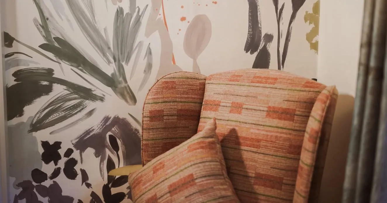 Patterned upholstered armchair with a matching cushion against a wall covered in abstract floral brushstroke wallpaper.