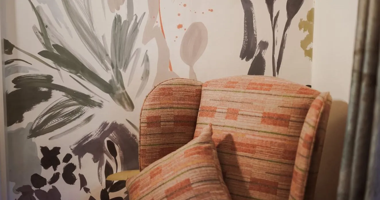 Patterned upholstered armchair with a matching cushion against a wall covered in abstract floral brushstroke wallpaper.