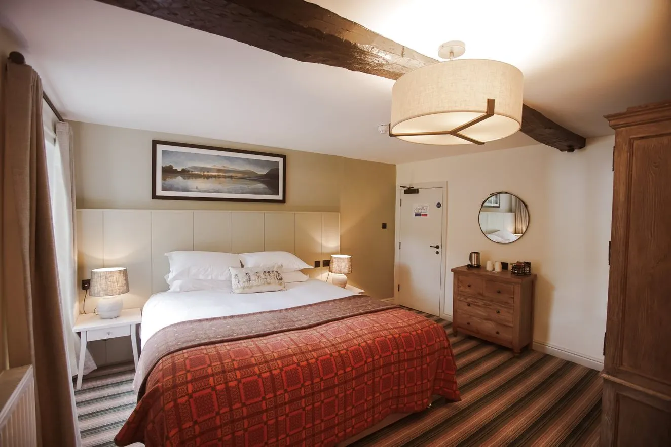 Cosy hotel bedroom with exposed wooden beams, double bed and red patterned bedspread.